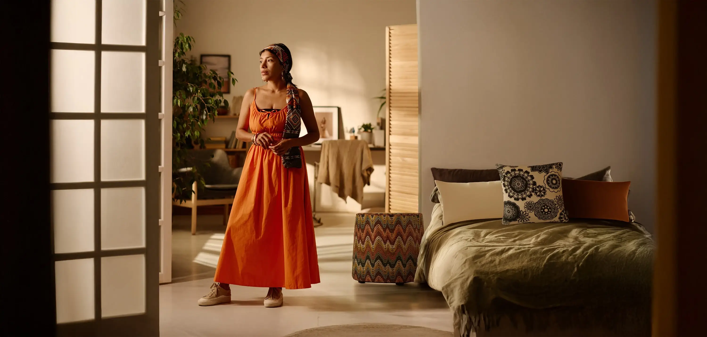 Frau in orangefarbenem Kleid steht in einem Zimmer mit Kissen und Pouf der Tulum-Kollektion von Rohleder.