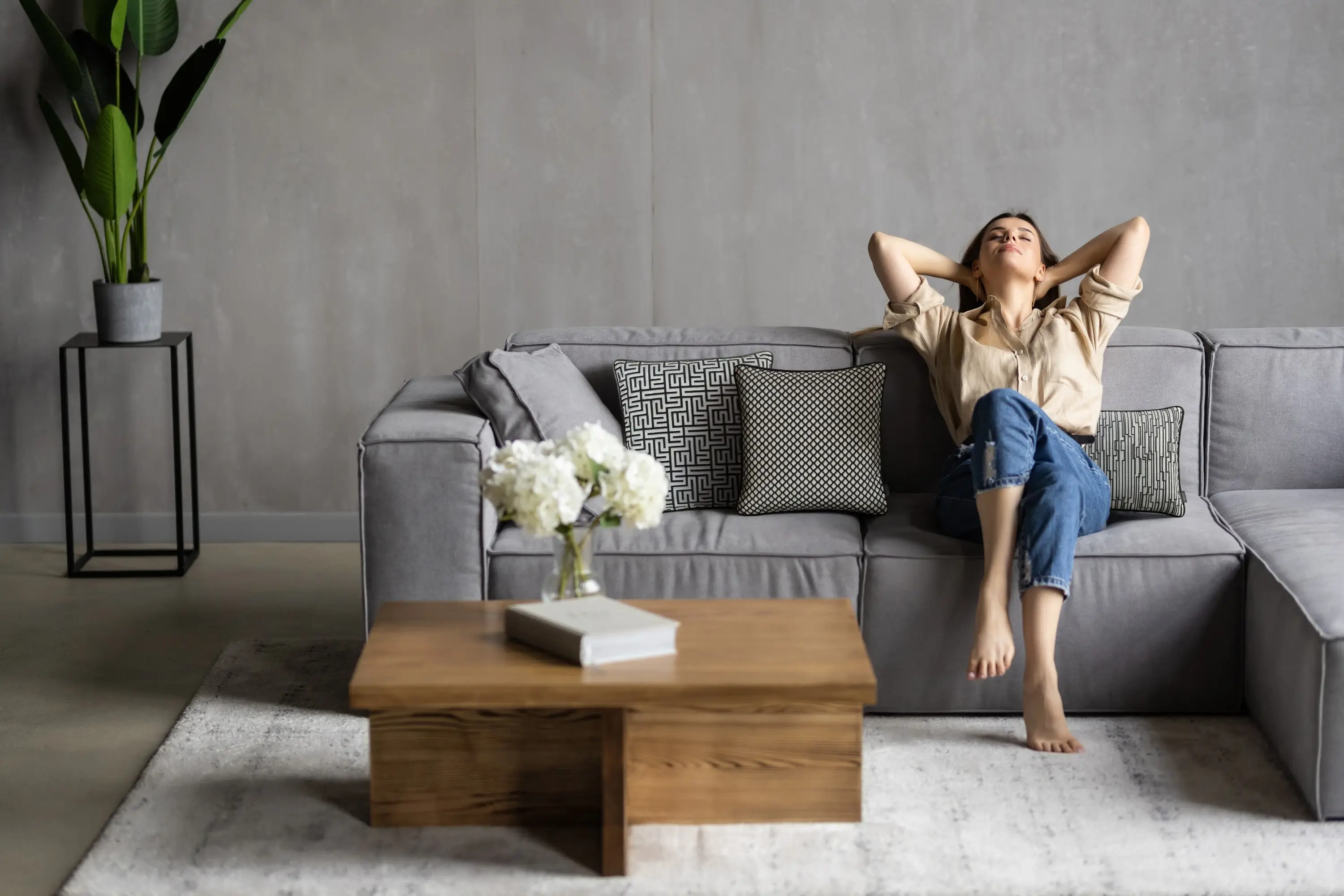 Frau entspannt auf grauem Sofa mit Kissen der Eternity-Kollektion von Rohleder.