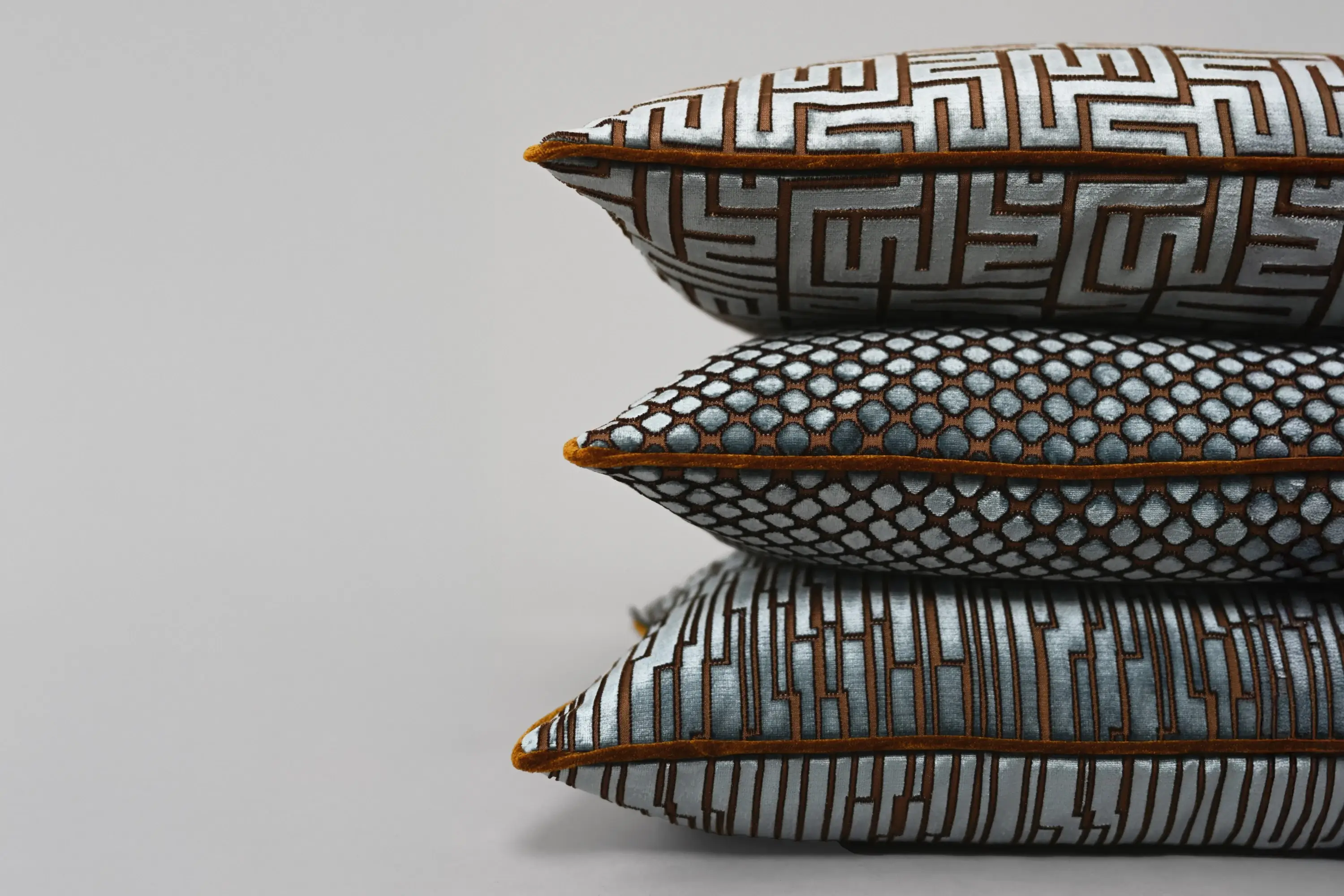 Gestapelte Zierkissen aus der Eternity-Kollektion von Rohleder mit grafischen Mustern.