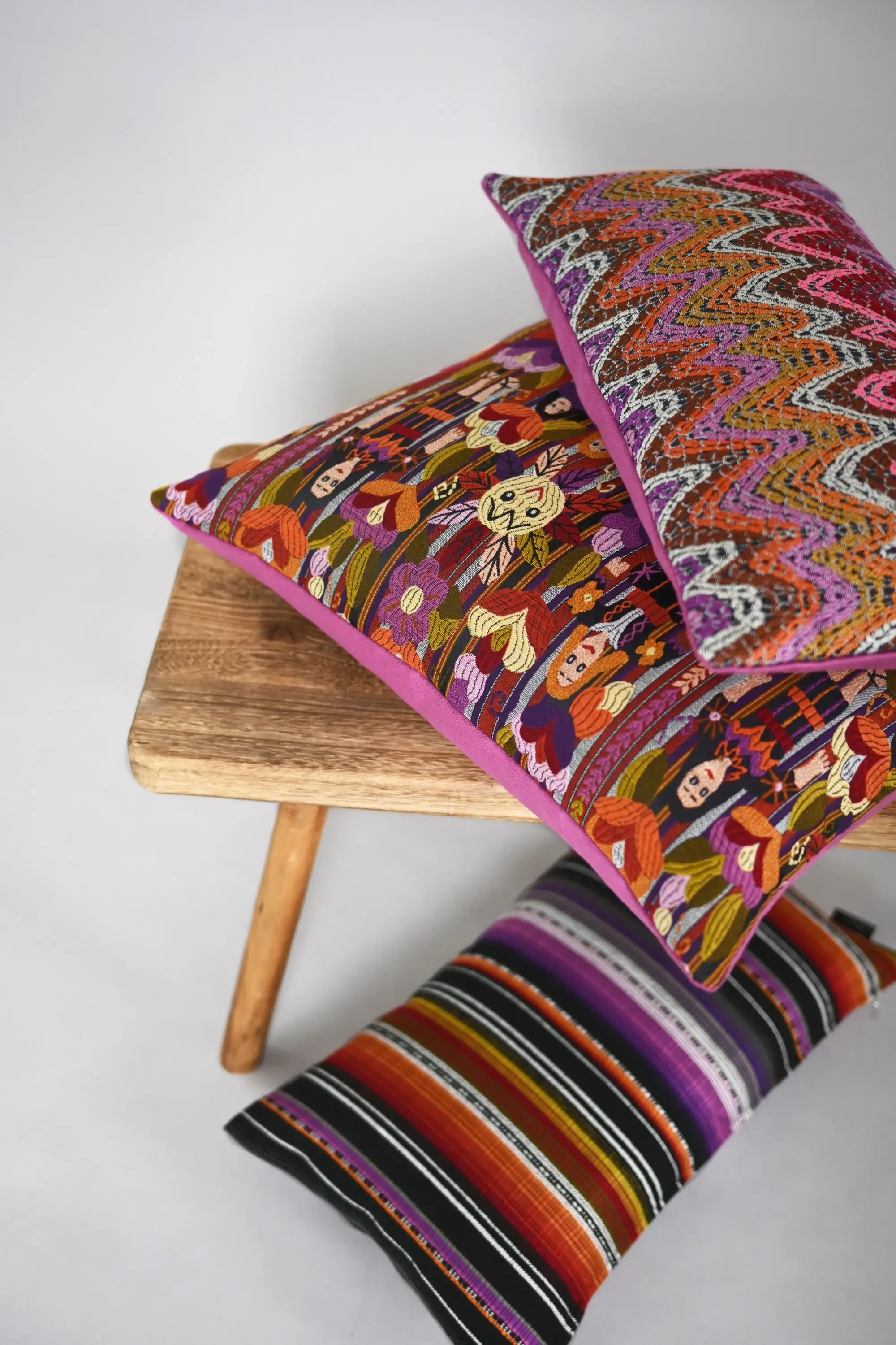 Bunte Kissen der Tulum-Kollektion von Rohleder auf einem Holzschemel arrangiert.